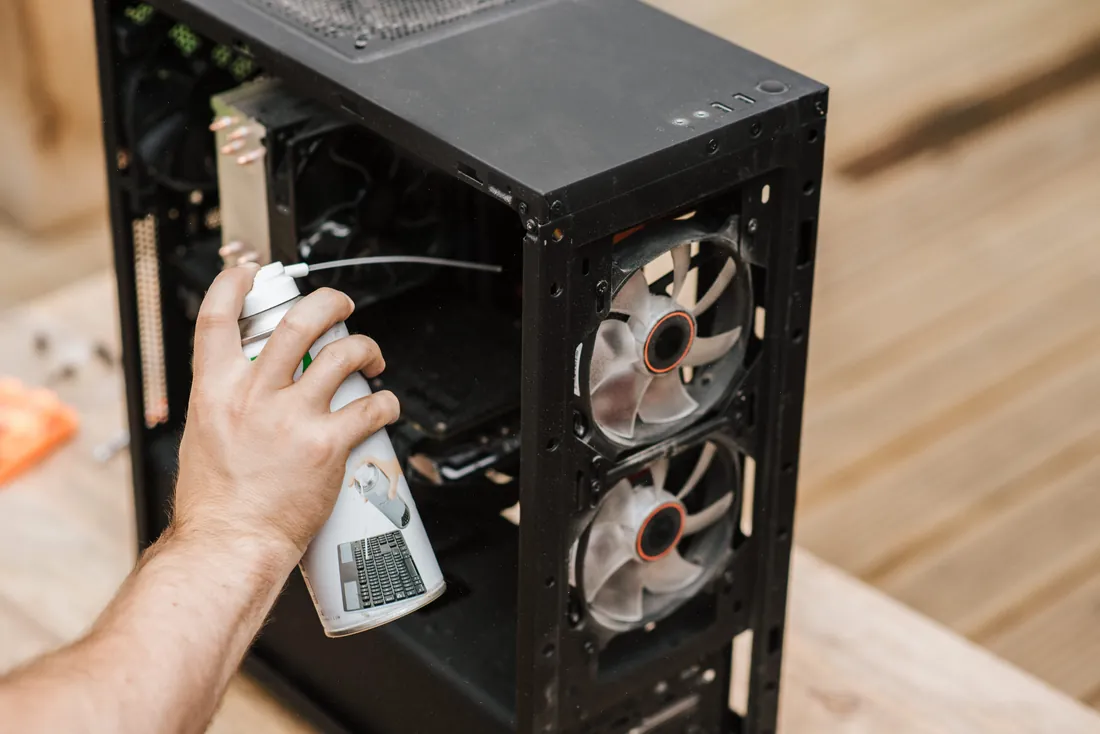 Une main nettoie à la bombe d'air une tour PC ouverte et poussiéreuse.