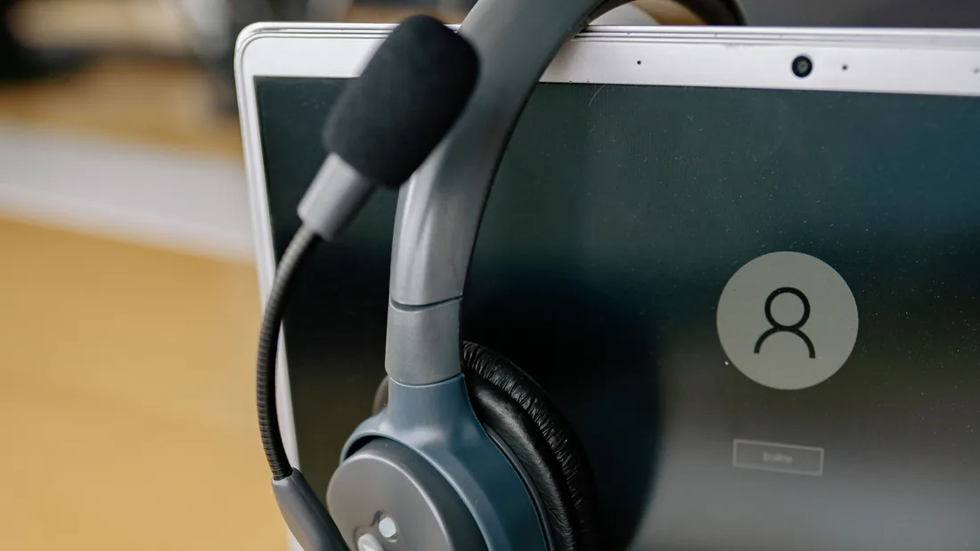 Un casque avec micro posé sur l'écran d'un ordinateur portable argenté.