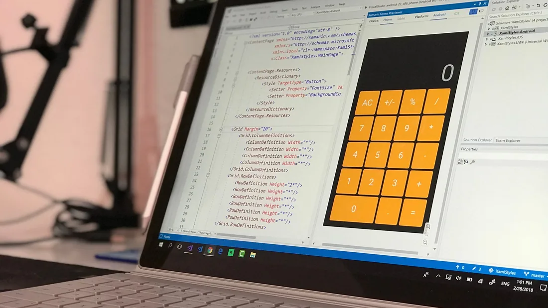 Écran d'ordinateur en gros plan, avec le code d'une application à gauche et, à droite, l'application en cours de création, une calculatrice à touches orange.