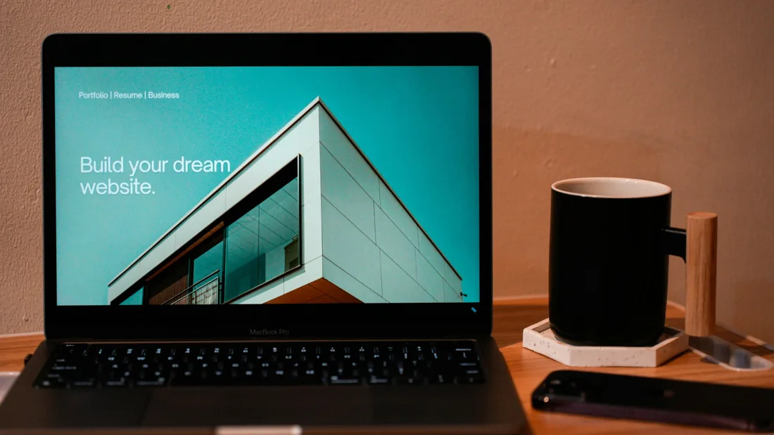 Ordinateur portable sur une table en bois, avec à l'écran la page d'accueil d'un site, à côté d'une tasse noire.