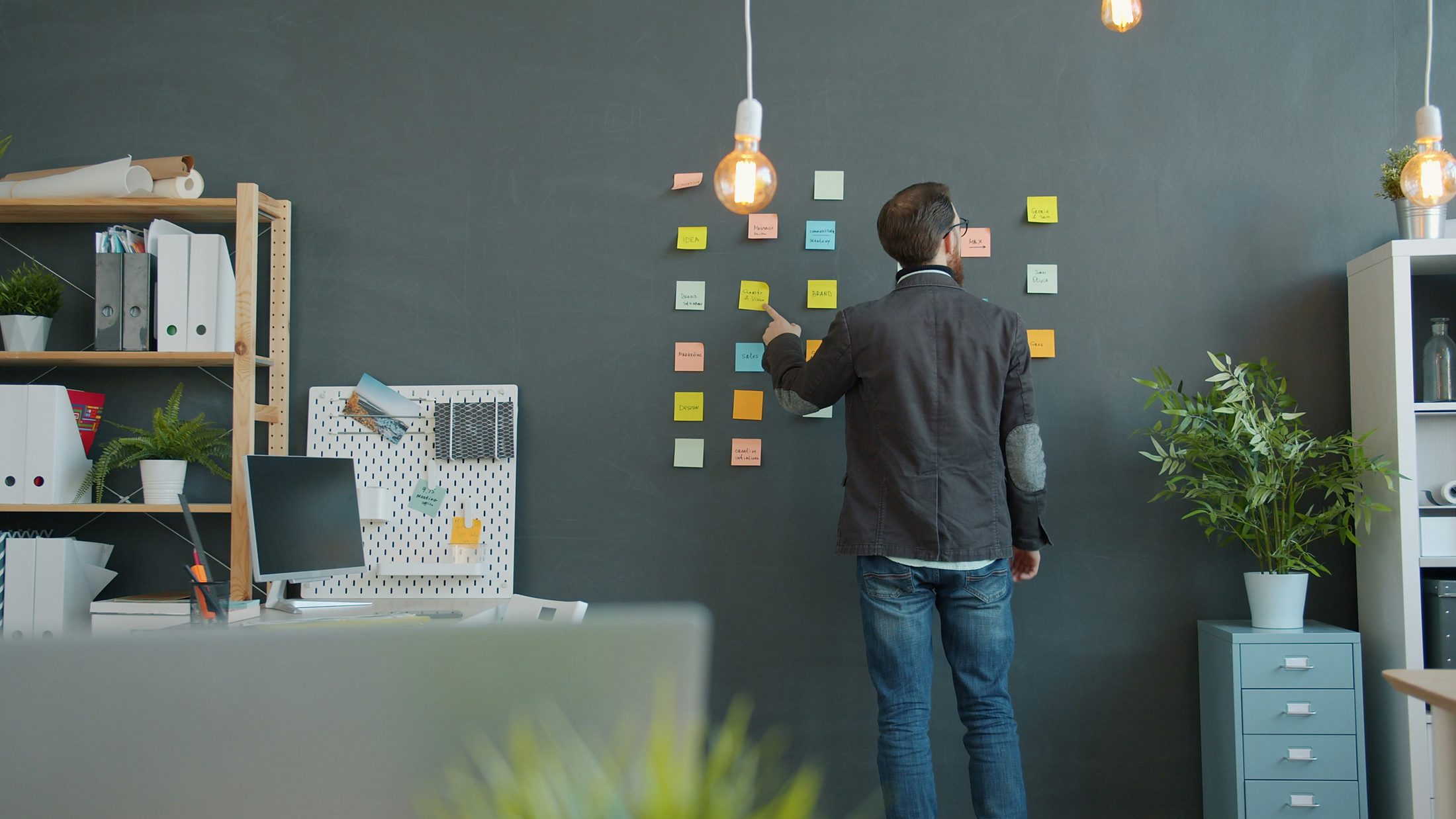 Un atelier de planification : des dizaines de post-its de couleur épinglés au mur, une personne de dos qui relie les idées une à une