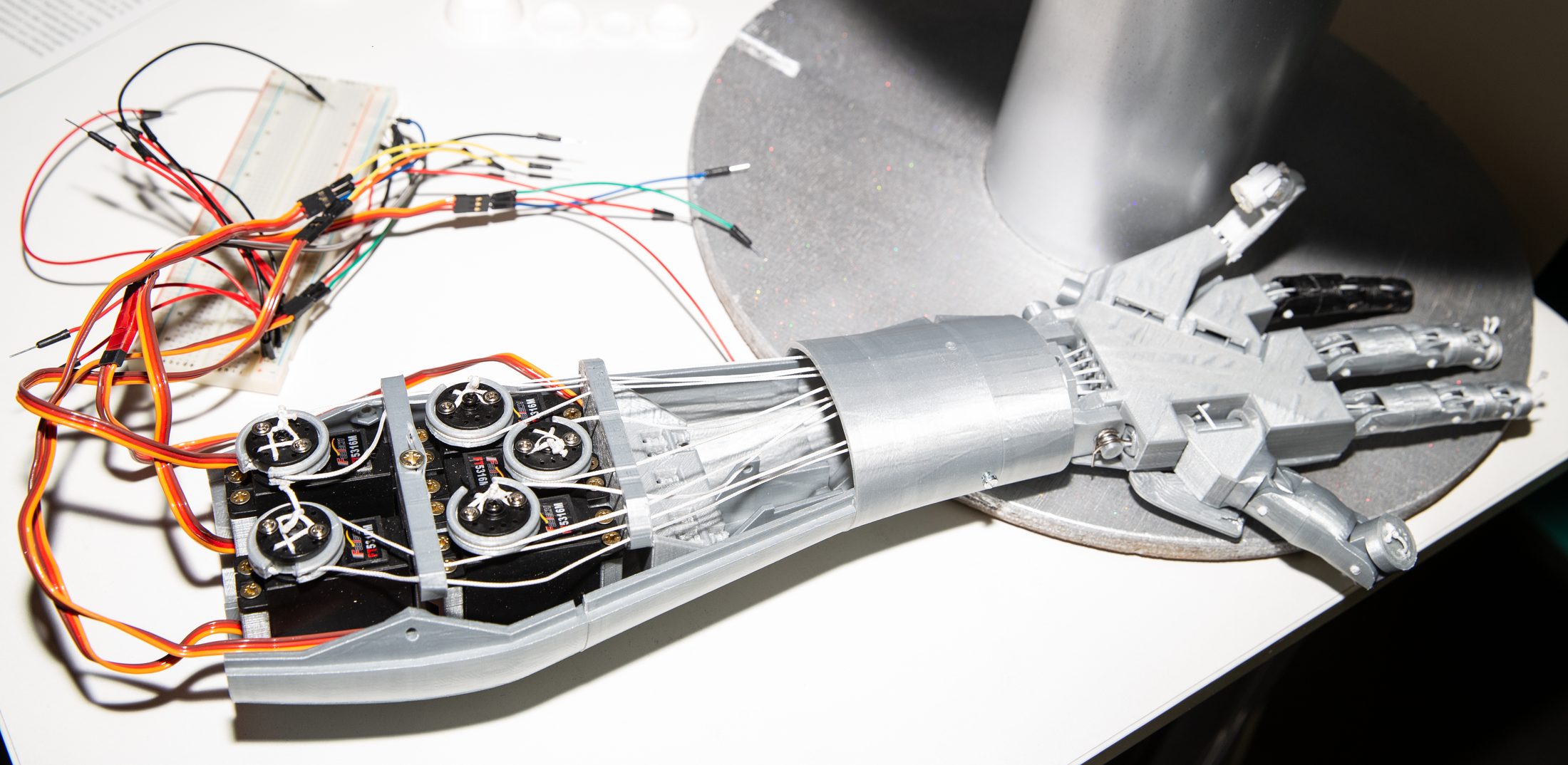 Main robotisée imprimée en 3D : un banc de servos relié à une platine d'essai tire des câbles-tendons qui traversent l'avant-bras jusqu'aux doigts articulés